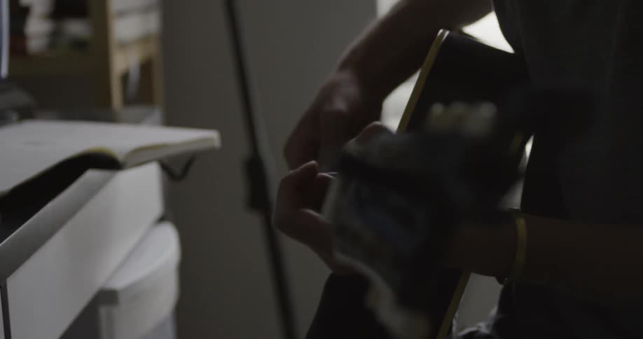Person strums a guitar sitting next to a desk