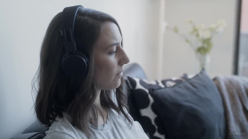 A woman is wearing headphones as she works on her couch in daylight