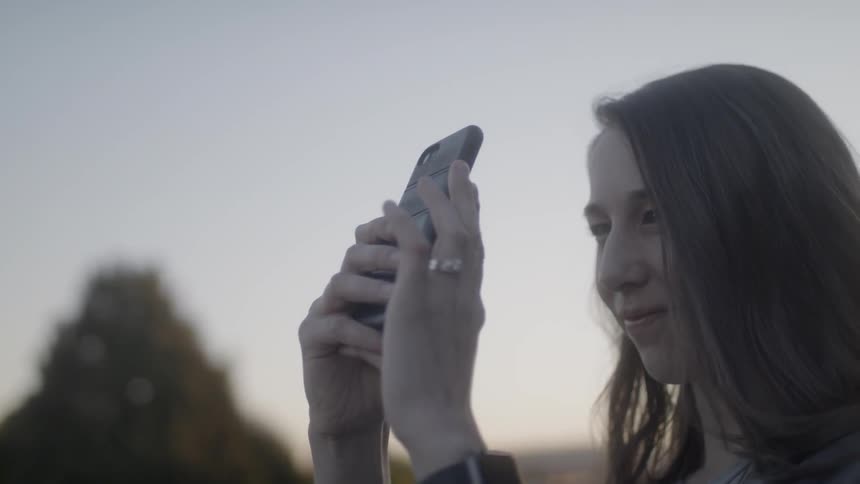 Woman holding up a phone and recording nature at sunset