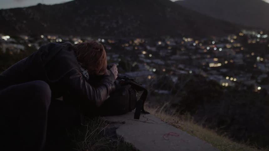 A man looks through his camera on a wall overlooking a village