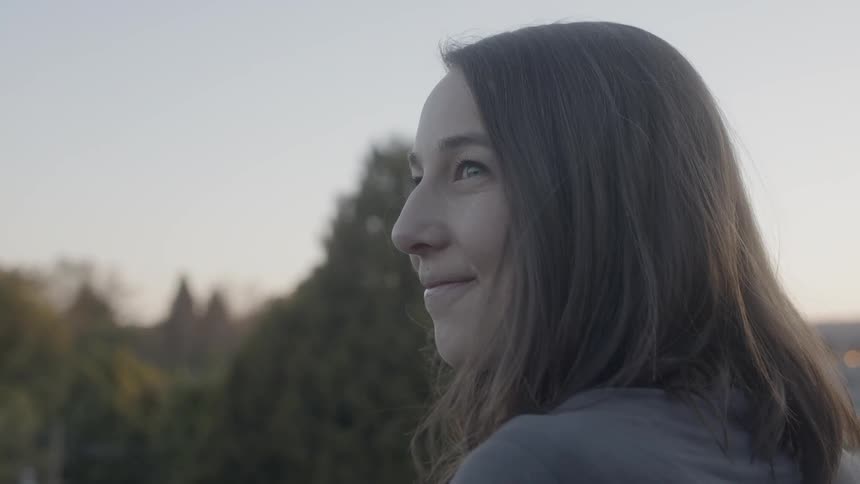 A woman is smiling as she stand outside taking in a view on clear day