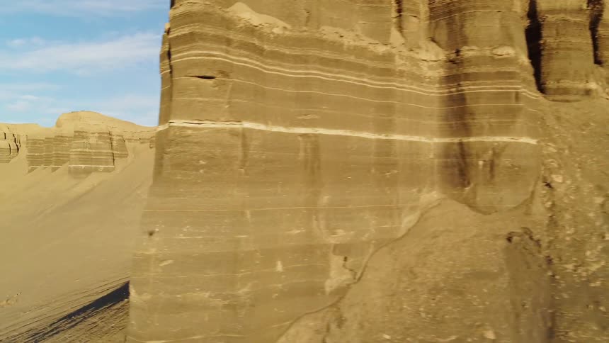 Sand and silt pile up at the base of canyon walls on a sunny day