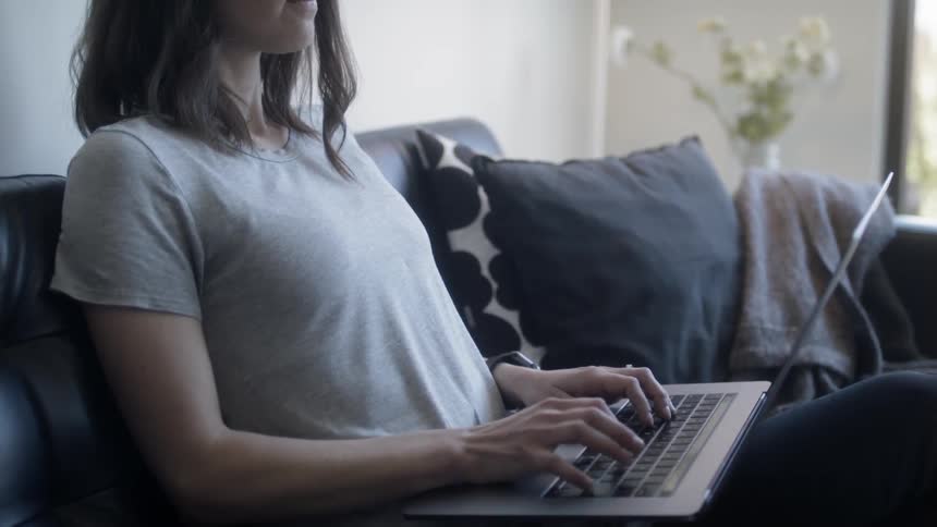 Woman sits on a couch typing on a laptop