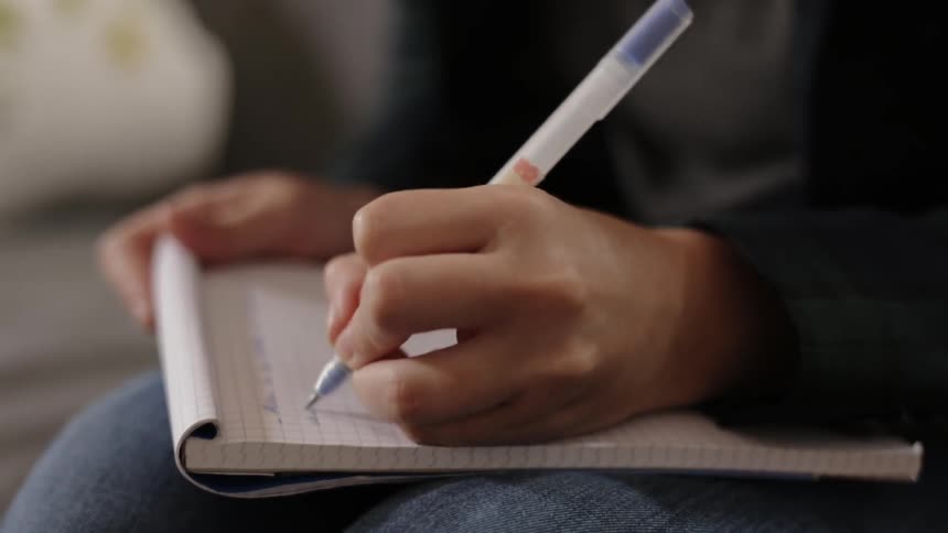 A woman writes on a notebook she's holding on her lap