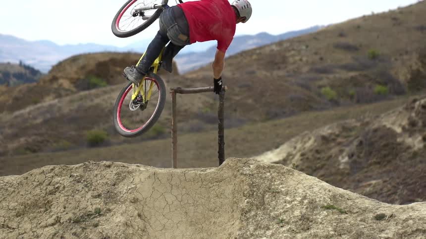 A young man riding a bicycle up a dirt hill and falling off as he jumps from the hill