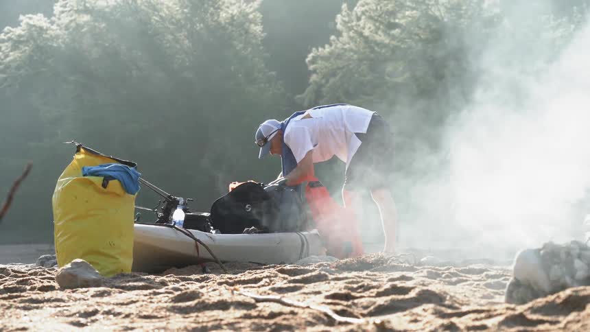 Person digs into a pack on a small canoe with smoke billowing nearby