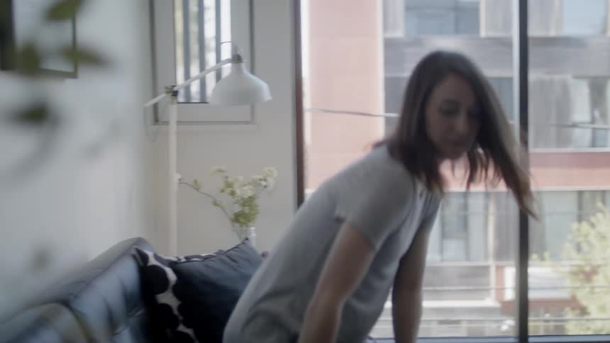Woman enters a room and sits on the sofa then opens a laptop