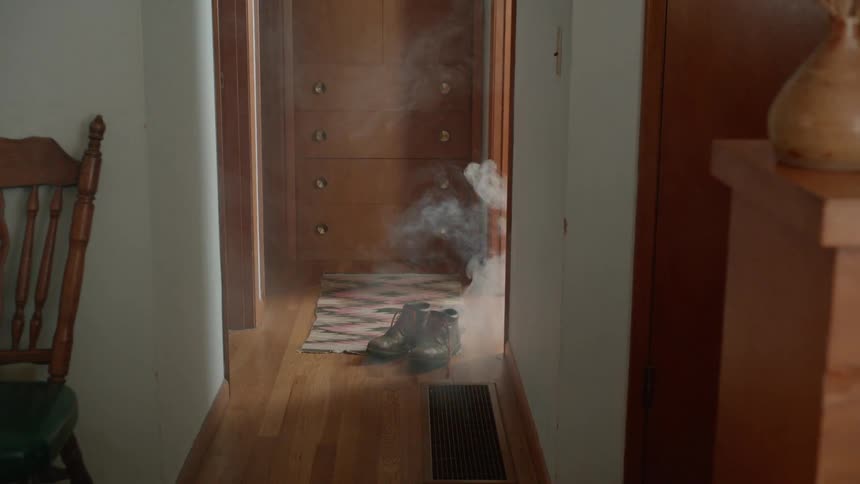 Smoke billows out from a room at the end of a hallway as a man emerges from the room