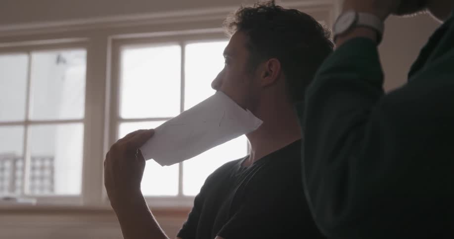 A man holds a paper over his mouth as another gestures with his hands