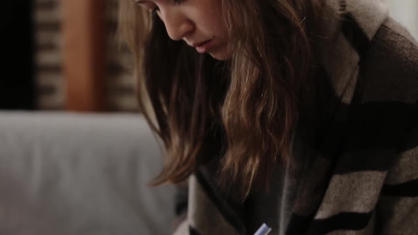 Woman is sitting on couch and writing in notebook