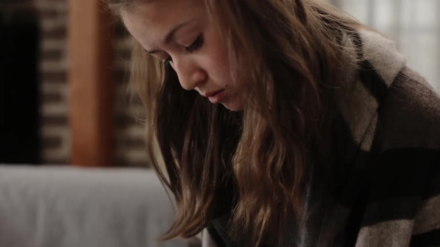 A woman writes in a notebook while sitting on the couch