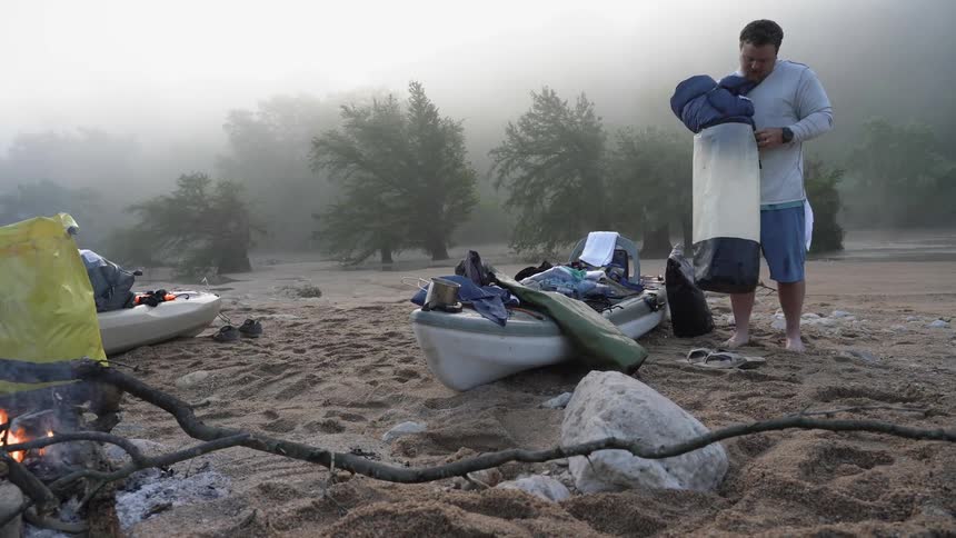 Man puts a sleeping bag in a bag at a campsite