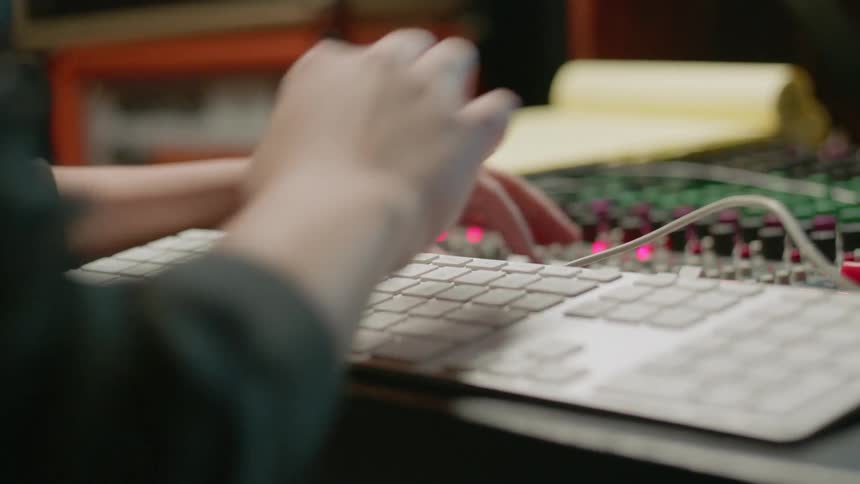 Person types on a keyboard and tunes knobs on a soundboard