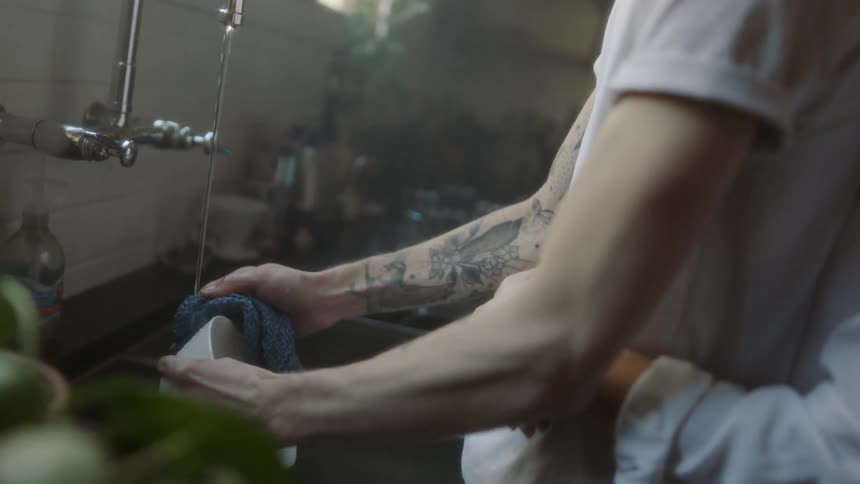 A woman is embracing a man as he is washing dishes at a sink in daylight