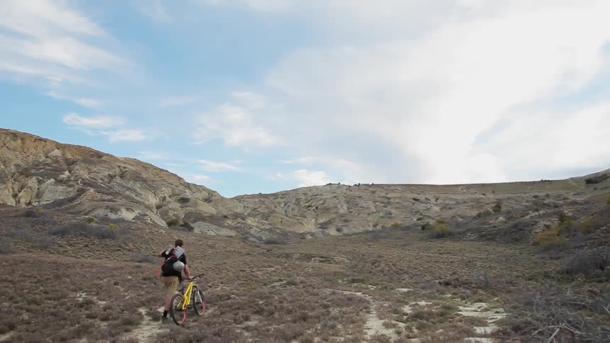 A person walking his dirt bike through scrub brush