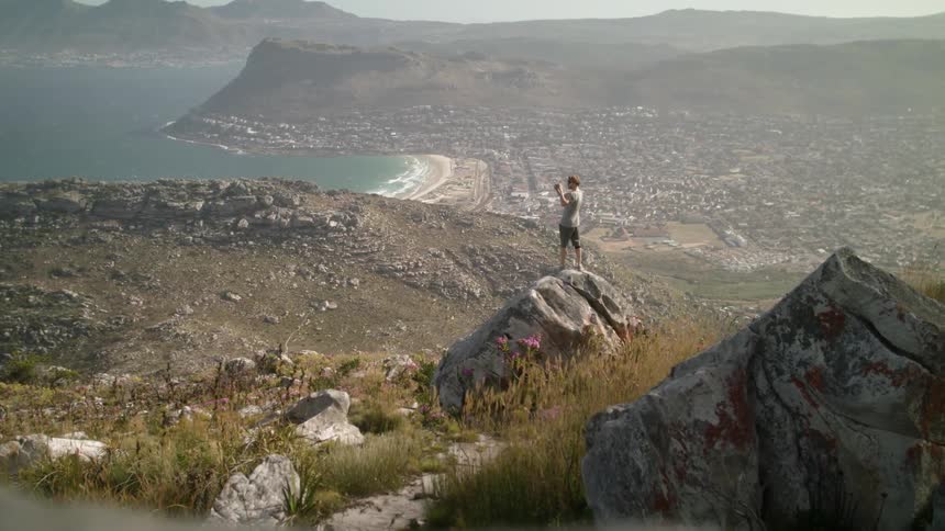 Man stands on a rock overlooking hills and water