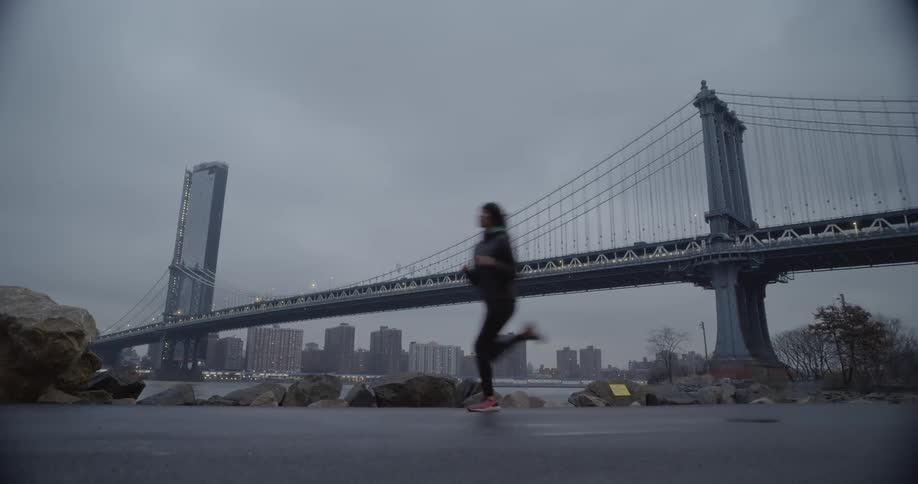 Woman jogs outside near a river and a bridge