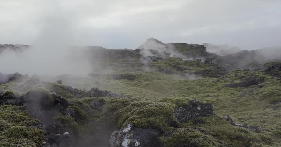 Smoke floats over the mossy rocks under a cloudy sky