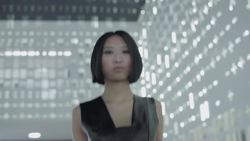 Woman walks near a wall with holes in it and light shining through