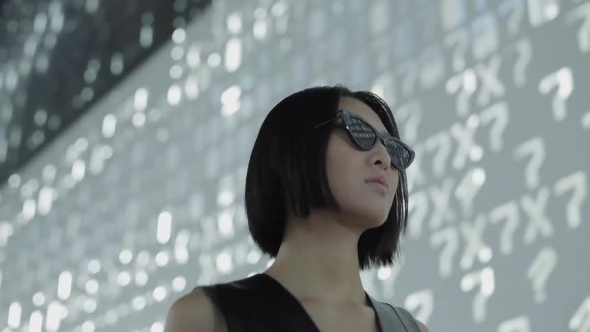 A woman wearing sunglasses walks past  a wall of lights