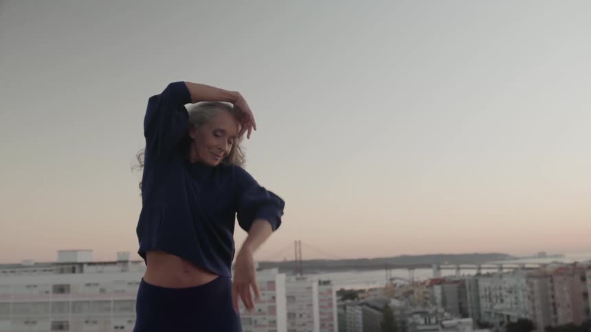 A woman dances and stretches on a rooftop at sunset
