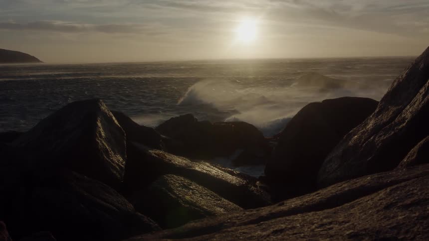 Waves crash into the rocks as the setting sun shines