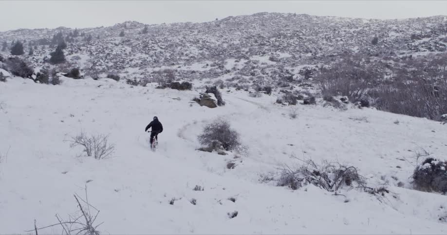 Someone riding a bike in the snow in a hilly area