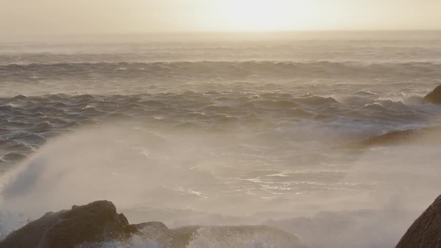 Waves are crashing against rocks at the beach on a windy day