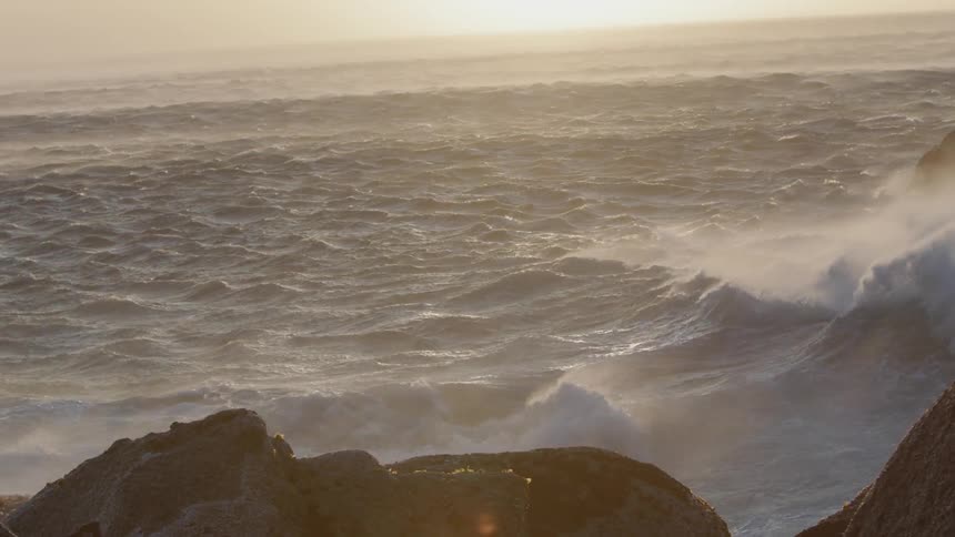 Wind blows the mist as ocean waves splash against the rocks