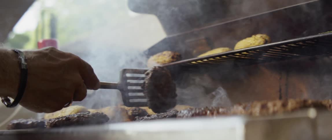 A man flips a burger on a flaming grill