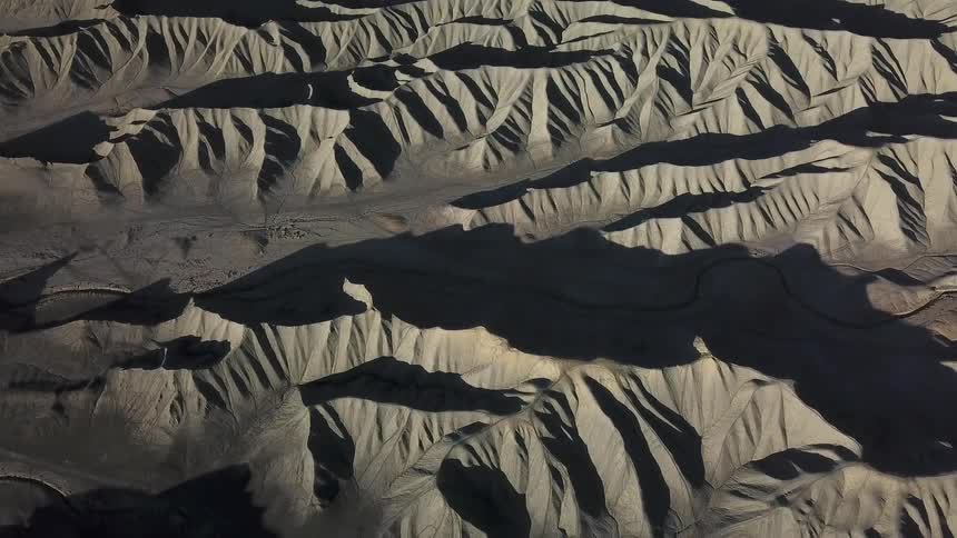 Shadows are clinging to the slopes of hills in a desert landscape during the day