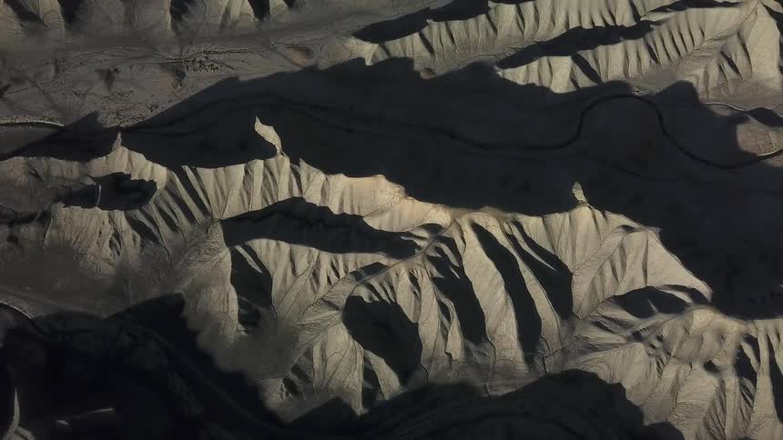 Shadows are clinging to the slopes of hills in a desert landscape during the day