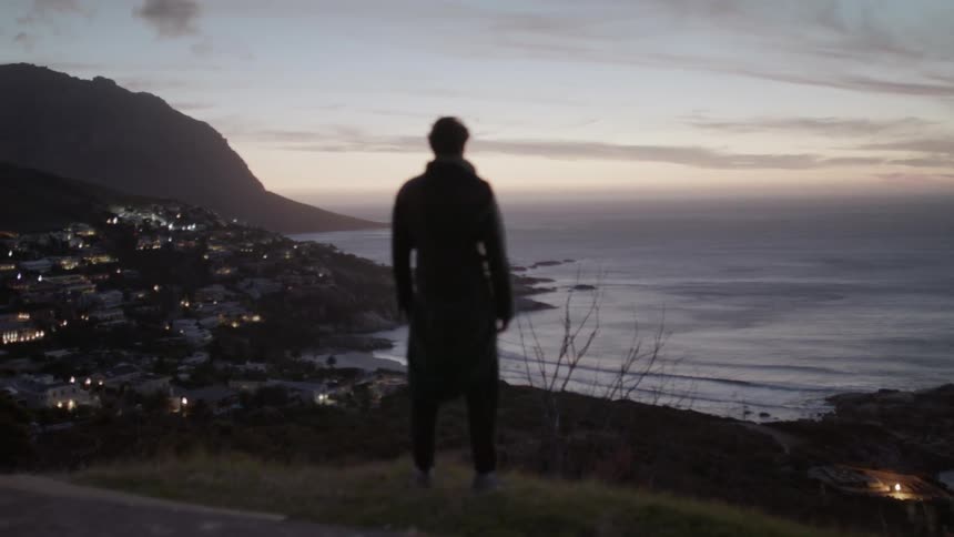 Man stands on a hill overlooking a body of water at sunset