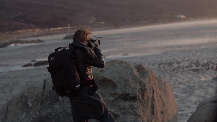 Man takes pictures of a body of water on a windy evening