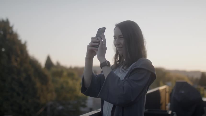 Woman takes a photo with her cellphone as she stands on a balcony