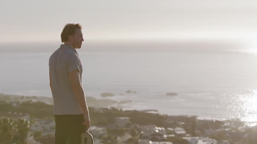 A man stands on a tall hill overlooking the town by the shore