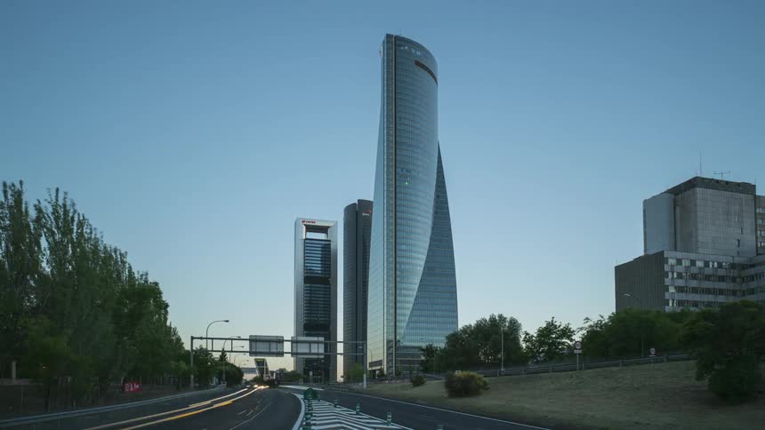 Traffic flows on a highway past skyscrapers as day turns to dusk