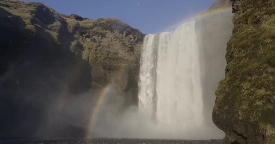 Waterfall gushes over a cliff near a rainbow