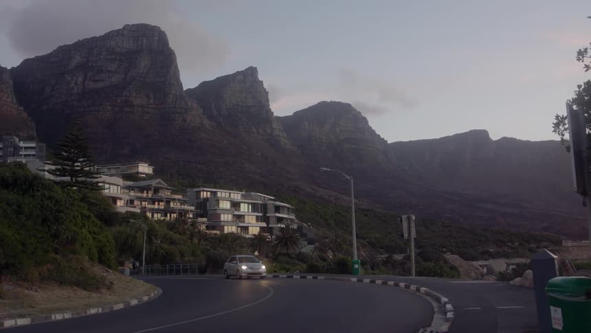 Car drives down a winding road near houses on a cloudy day