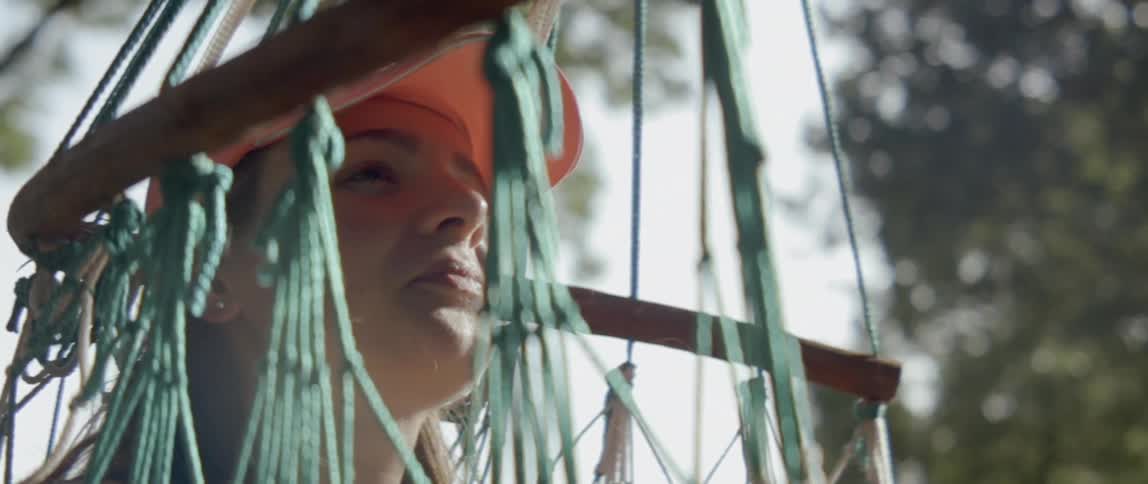 A woman sitting in a hammock looks up at the trees