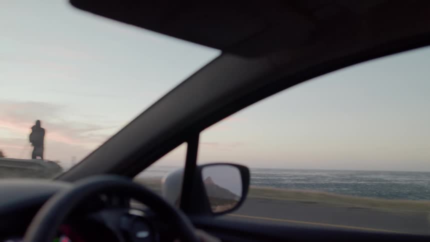 A person drives on a coastal road at sunset