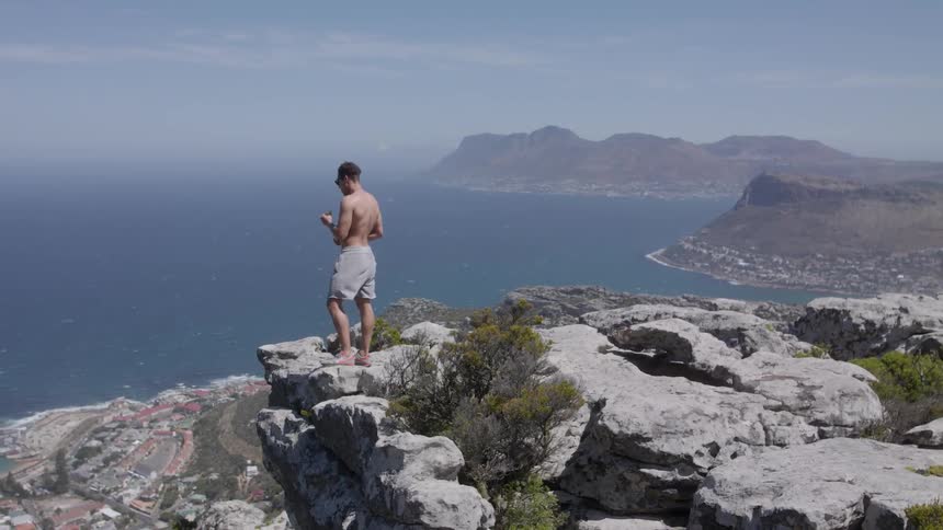 A man stands on top of a rock overlooking the ocean