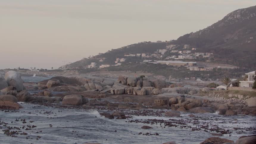 Ocean waves roll over rocks near shore and the wind blows mist
