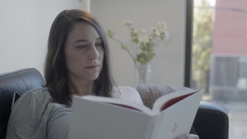 Woman sits on a couch reading a book