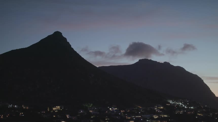 Lights in a town at the base of a hill glow at sunset