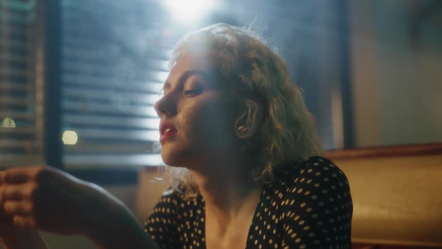 A light shines through a window on a woman sitting in a diner booth