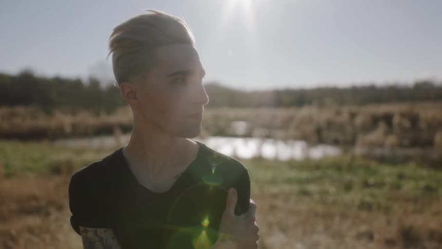Man stands outside on a sunny day near a small pond