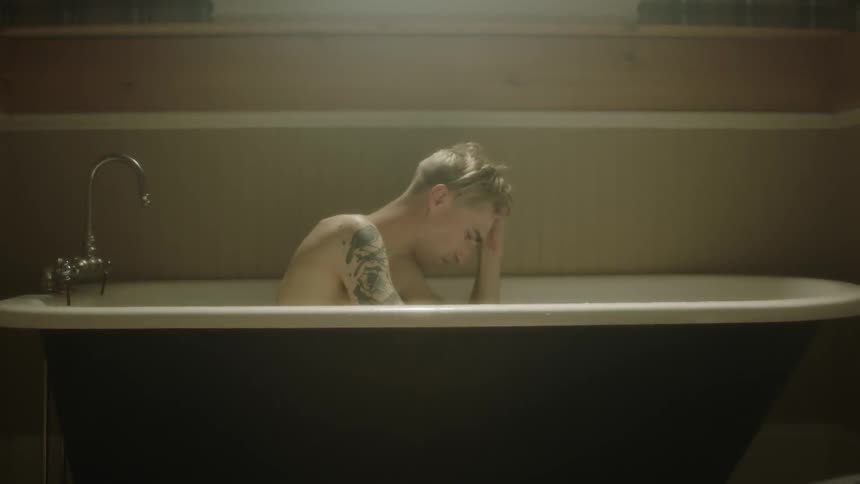 Man sits in a bathtub with a hand on his head