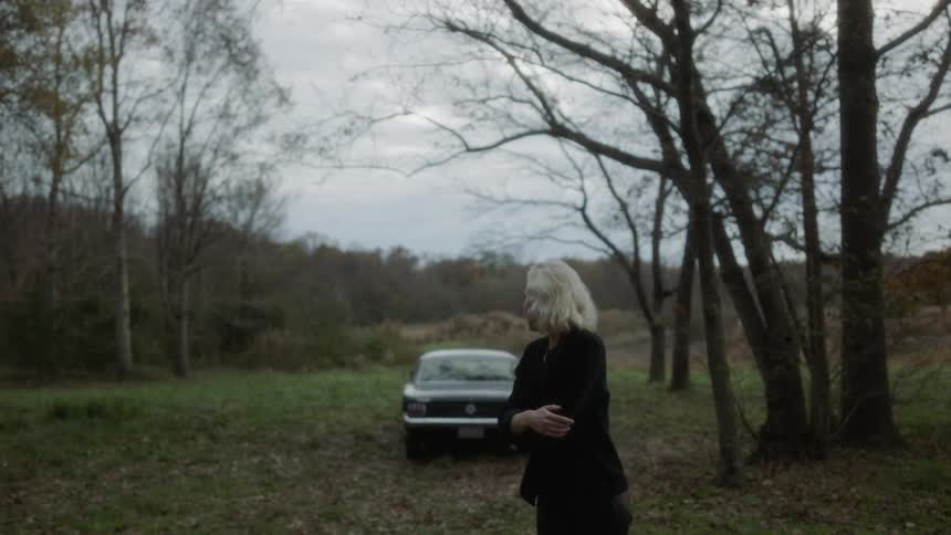 Woman walks away from a car in the woods on a cloudy day