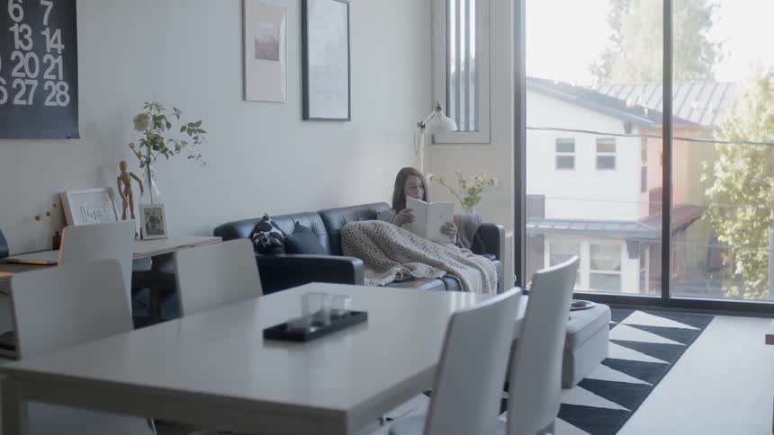 Woman sits on a couch covered with a blanket reading a book
